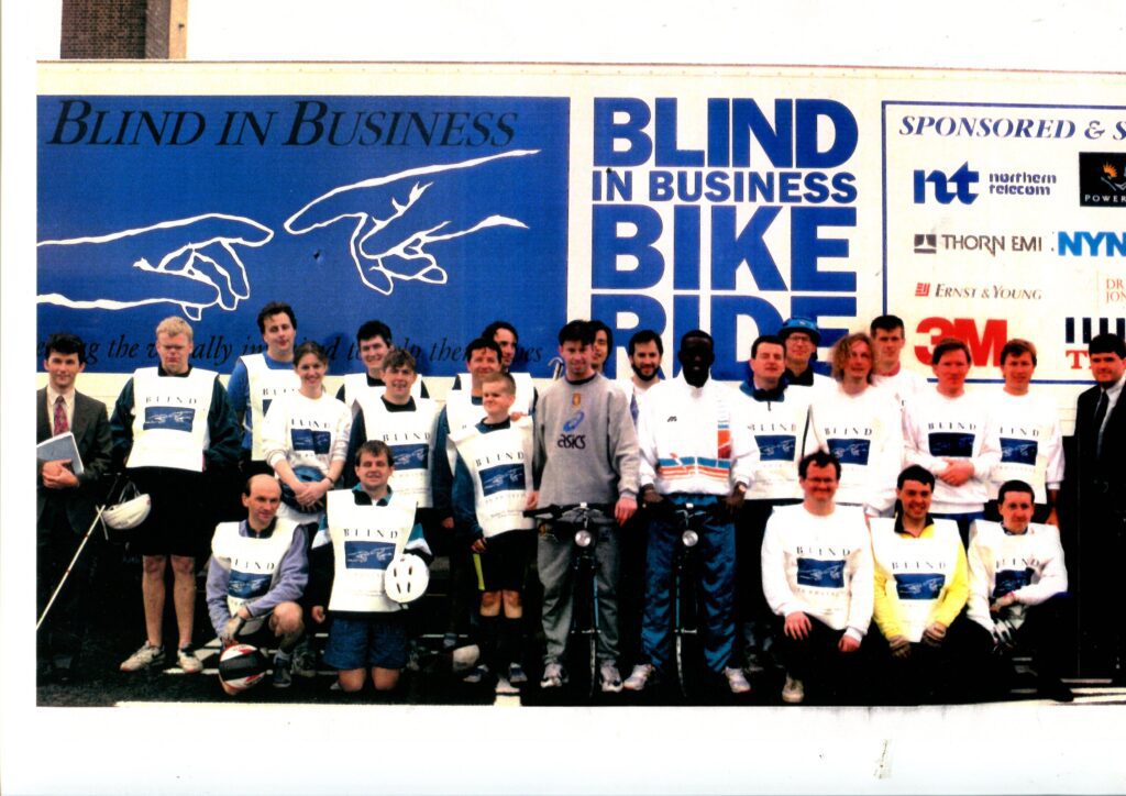 A large group of people smiling in front of a large Blind in Business sign.